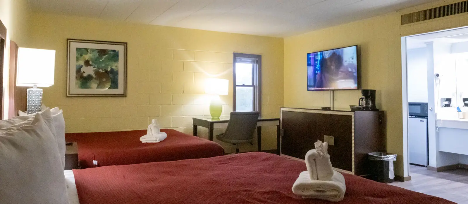A hotel room with two beds, a desk, a wall-mounted TV and a kitchenette area with a microwave and a mini-fridge