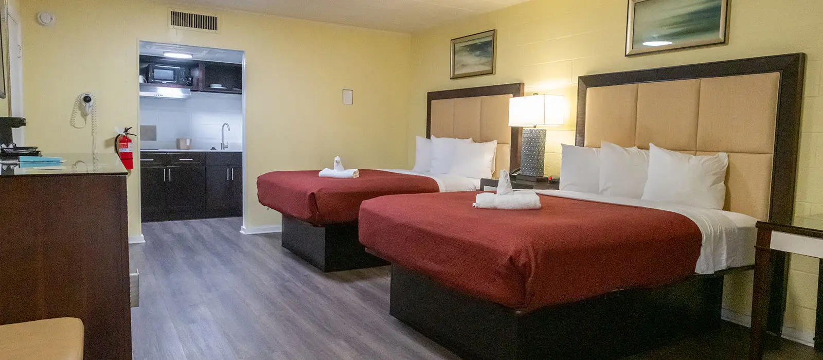 A guest room with two beds, a small kitchen area, and a fire extinguisher on the wall