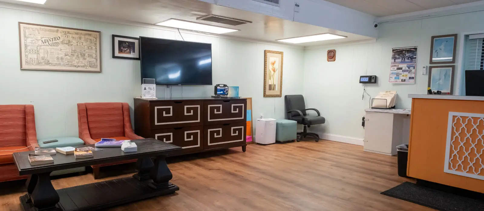 A waiting area with two orange chairs, a dark wood coffee table, a large TV, and an orange reception desk