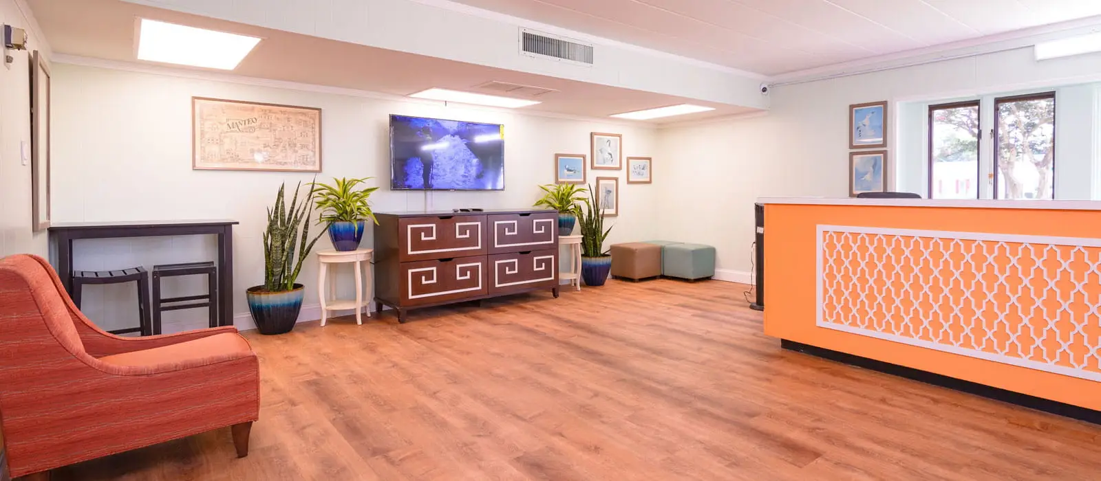 A hotel lobby with a bright orange reception desk, a television, and several potted plants