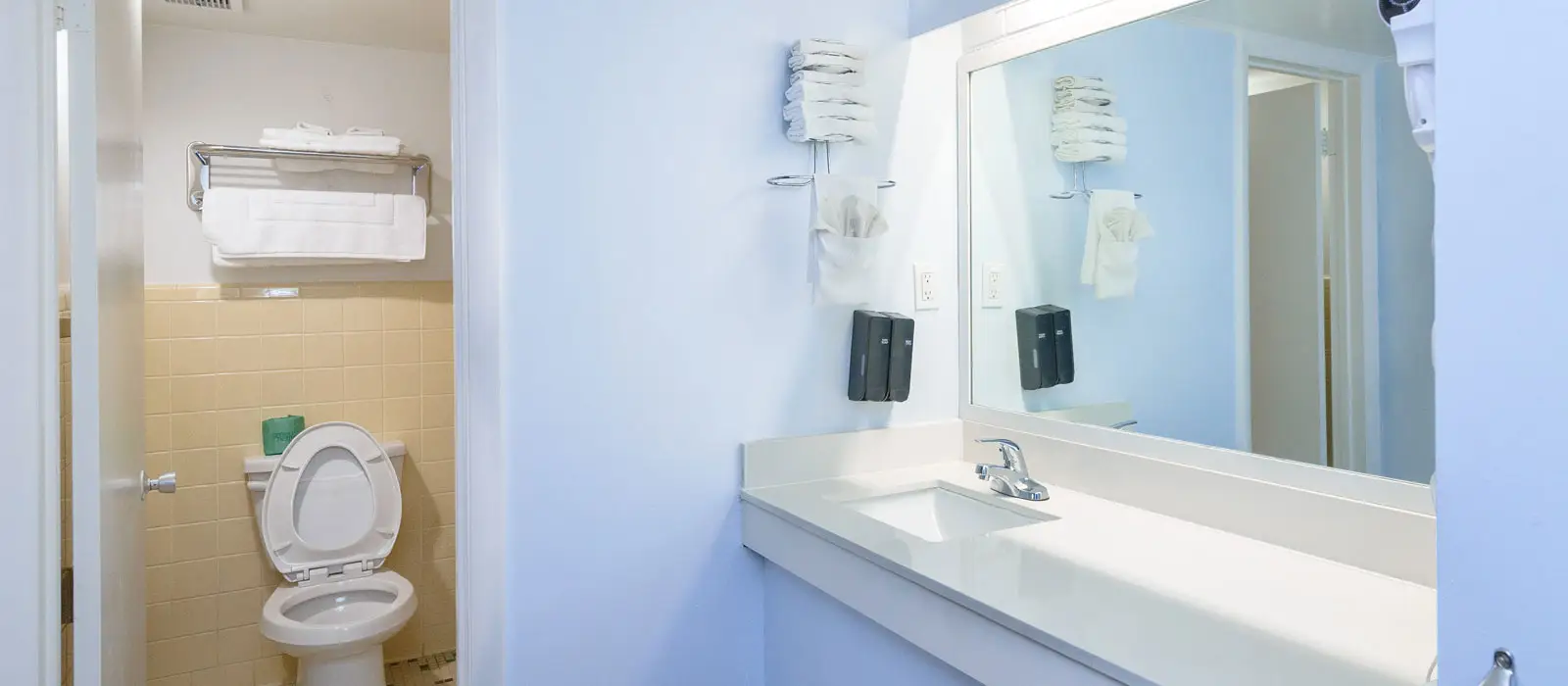 A bathroom with a white toilet, a white vanity with a sink, a mirror, and white towels on a rack