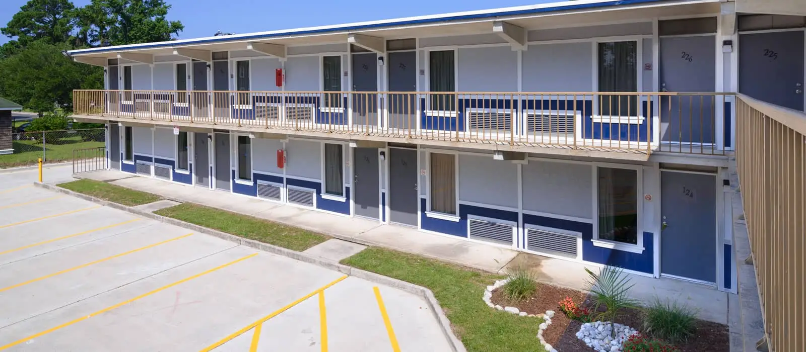A two-storey motel building with a parking lot in the foreground and trees in the background