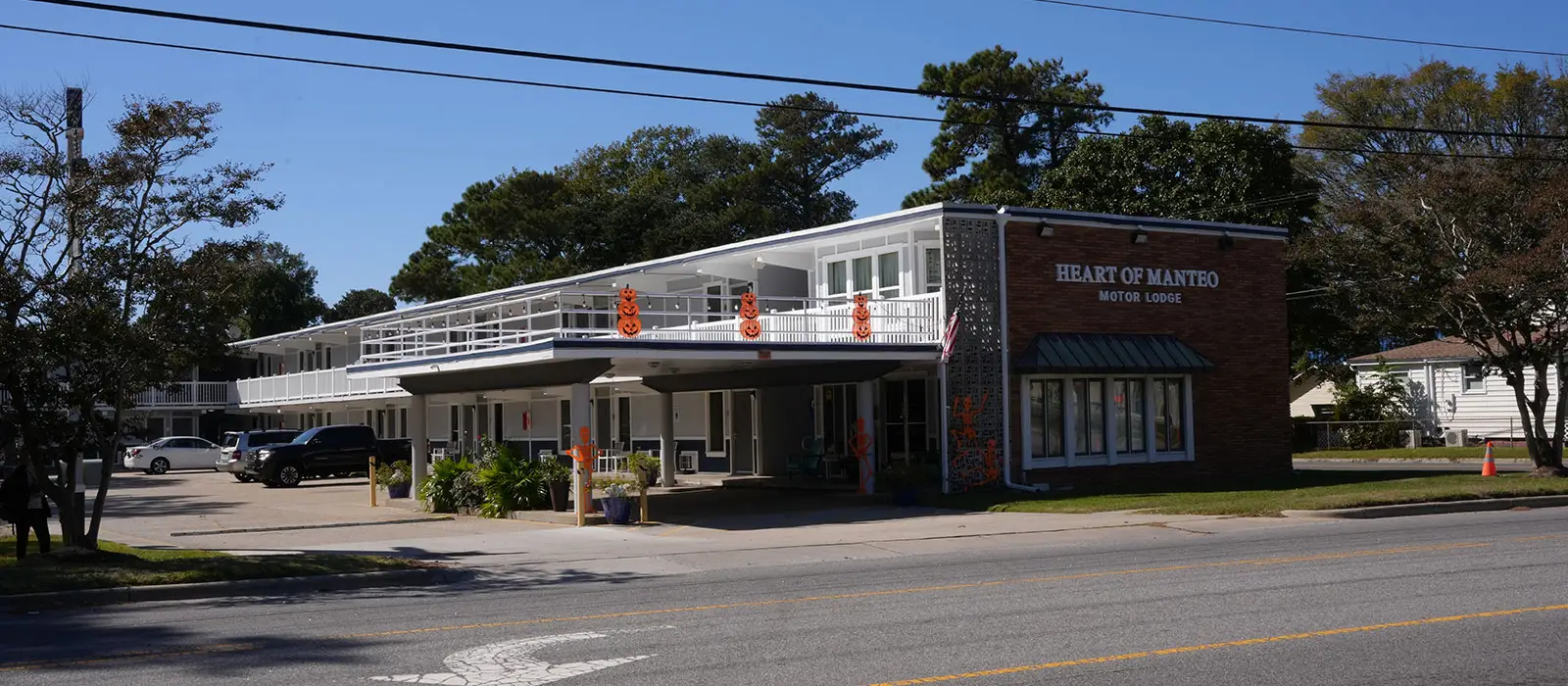The two-storey white motel building with a brick facade on the right has "HEART OF MANTEO MOTOR LODGE" written on it
