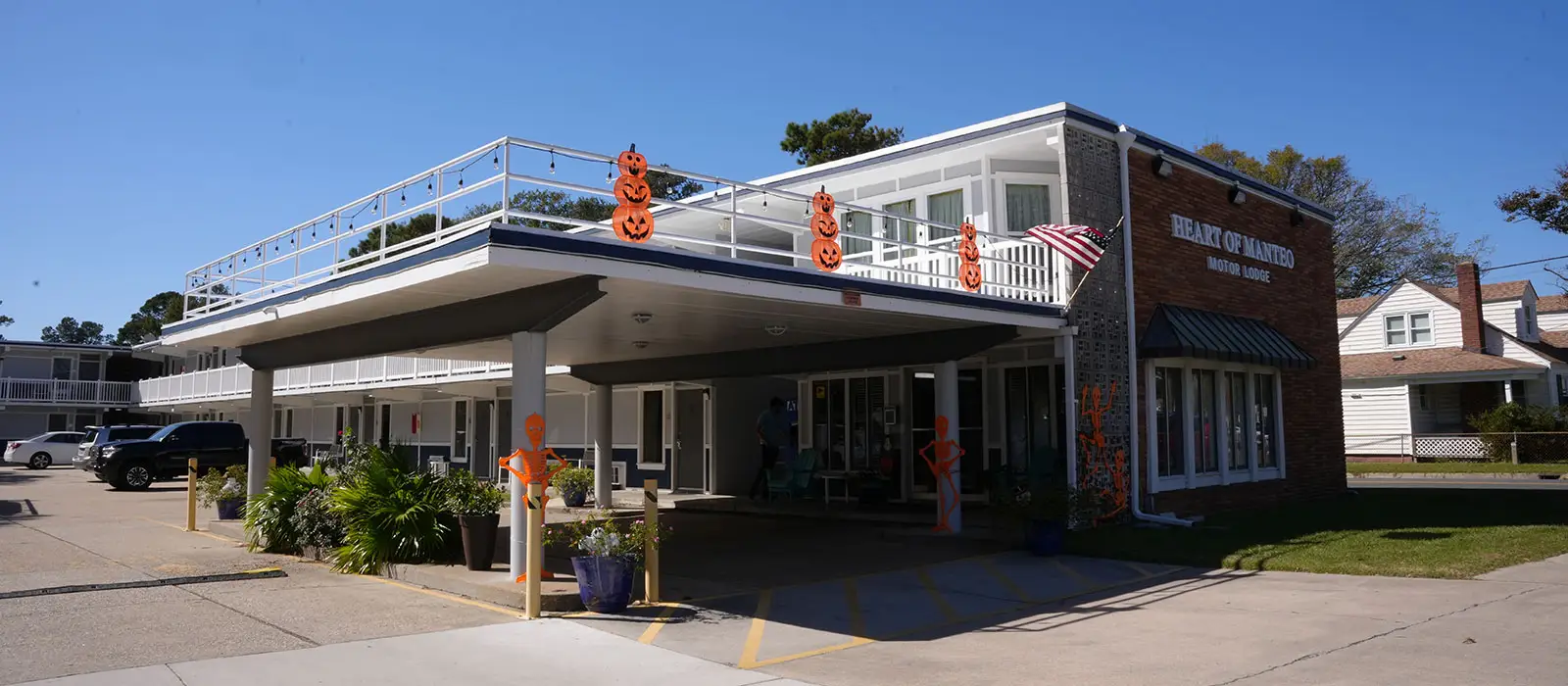 The two-storey building with a flat roof has a sign that reads "HEART OF MANTEO MOTOR LODGE" and is decorated with Halloween pumpkins