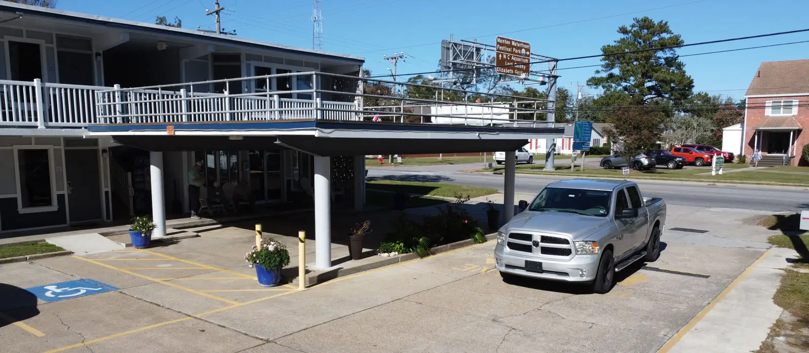 A two-storey motel building with a second-floor balcony walkway, a silver pickup truck and a street sign for "Hertford Waterfront Festival Park"