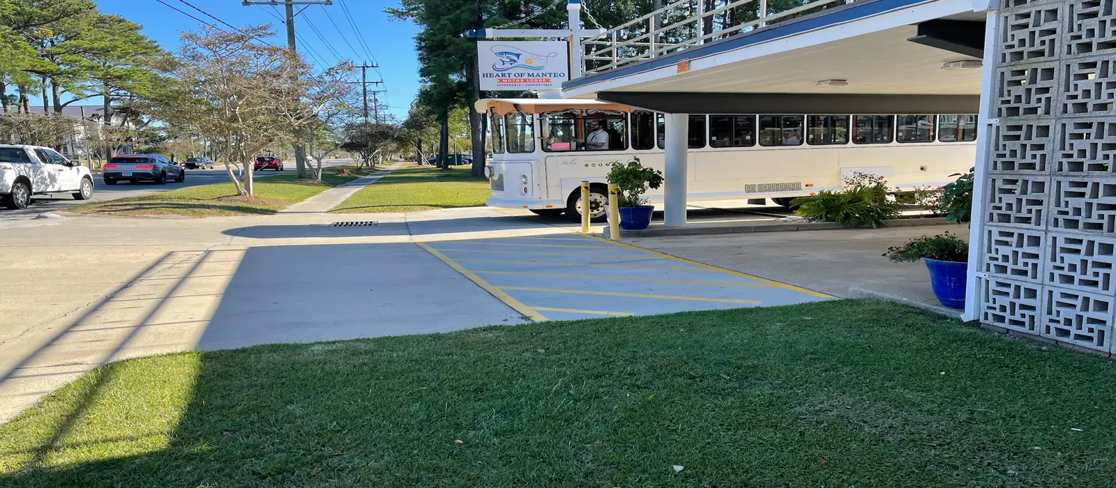 A white trolley bus is parked under a covered entrance next to a sign that reads "HEART OF MANTEO"